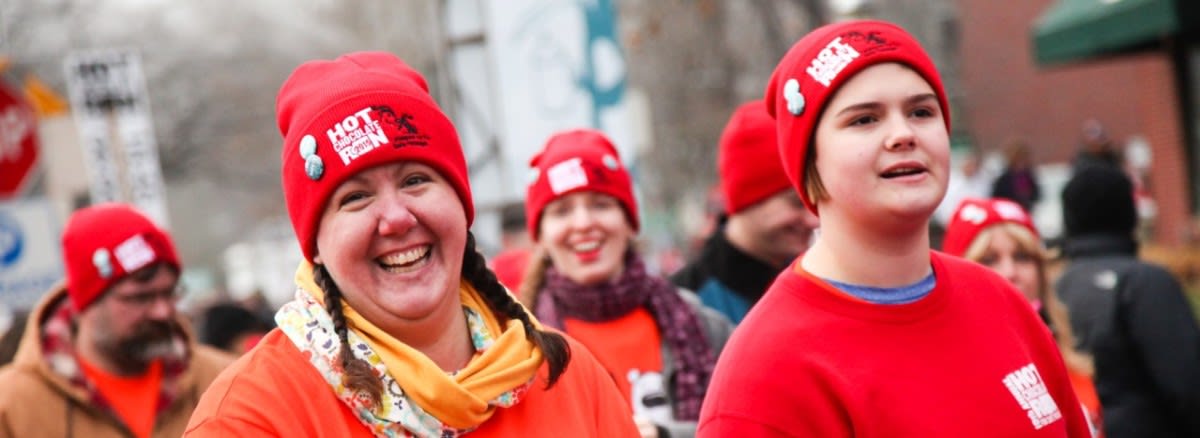 A crowd of people wear red hats with the Hot Chocolate Run polar bear and penguin logo.