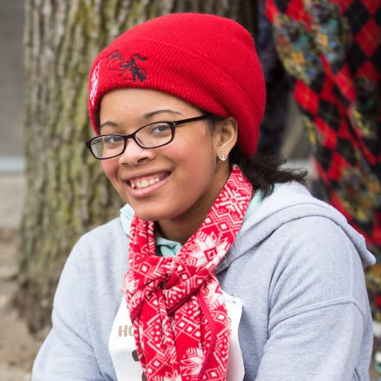 A smiling woman wears a matching red hat and scarf.