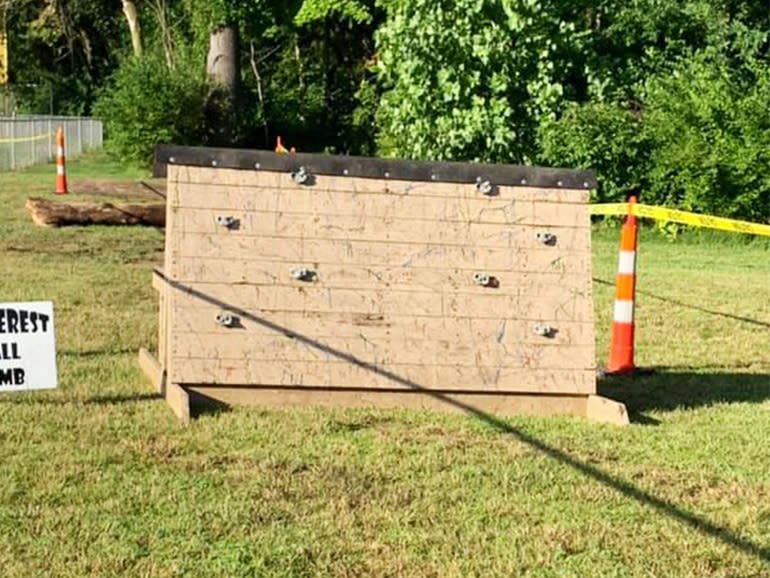 A wooden angled wall with wall climbing steps that is about 4 feet tall