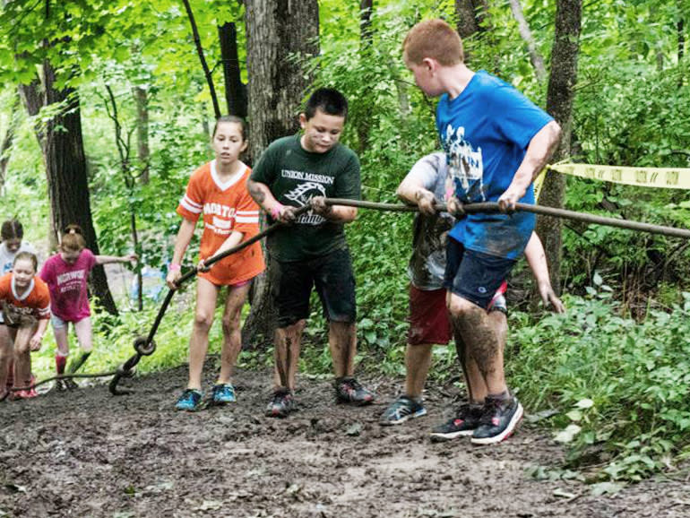 A group of kids making their way through the woods with the guidance of a rope