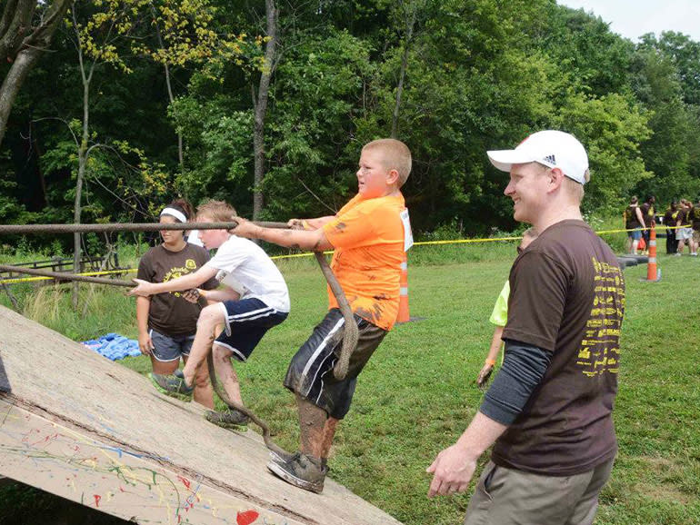 An angled wood shaped like a pyramid with kids pulling themselves over with a rope