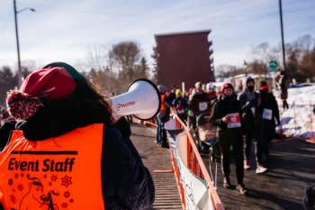 A volunteer wearing an orange vest calls to a group of walkers through a megaphone.