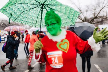 A woman dressed as the Grinch waves from under a green umbrella. She wears a red bib with the number 24.