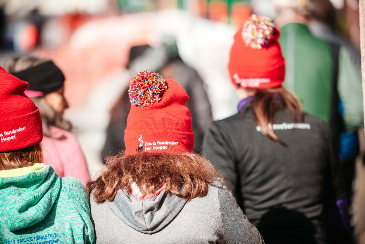 Three people walk wearing red hats with I'm a fundraiser for hope written on the back