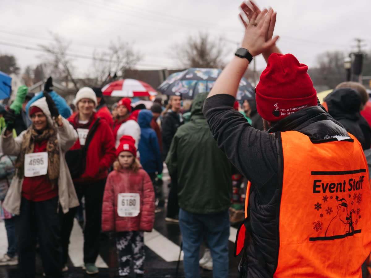 A volunteer wearing an orange vest cheers on a group of walkers.