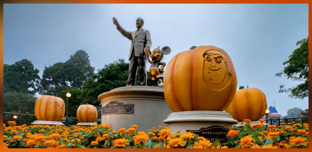 Statue of Walt Disney and Mickey Mouse surrounded by large decorated pumpkins and orange flowers during Halloween at Disney park