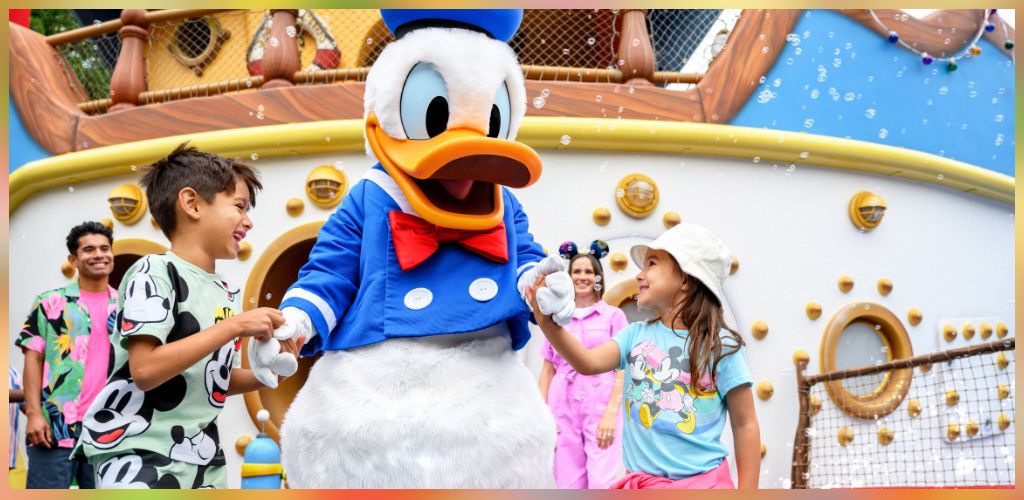 Children happily dancing with a mascot dressed as Donald Duck in front of a colorful, themed attraction at a fun amusement park.