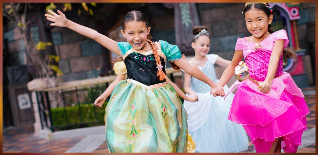 Group of young girls in colorful princess costumes smiling and holding hands outdoors at a celebration or party