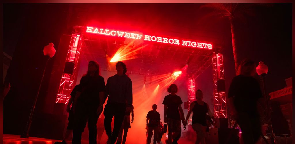 People walk through a haunted house with red lighting and a sign that says Halloween horror nights.