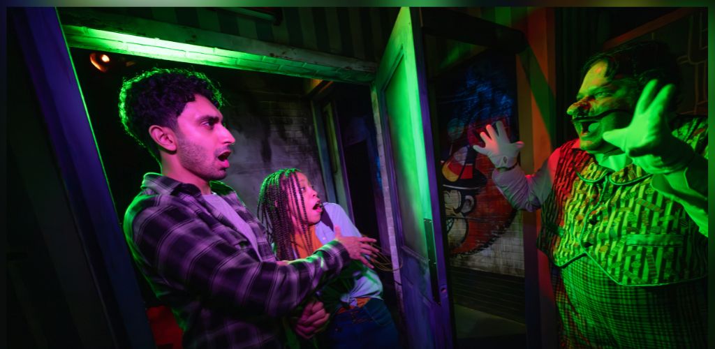 People reacting with excitement and fear to a clown in a haunted house attraction with colorful lighting and spooky decor