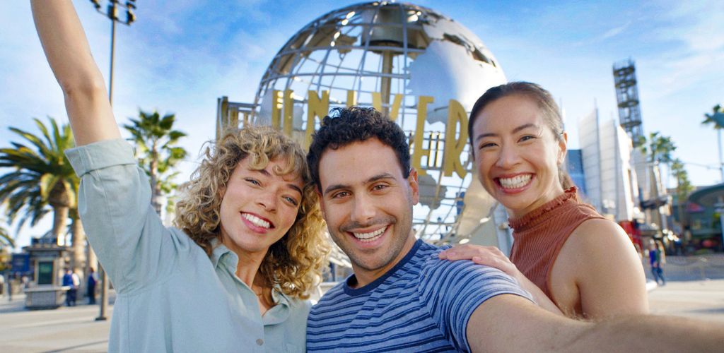 Group of friends smiling and taking a selfie in front of a globe sculpture at a theme park