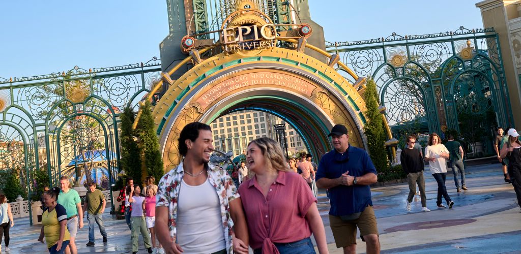 People walking out of the owners gate at universal studios during daytime with a large decorative arch in the background