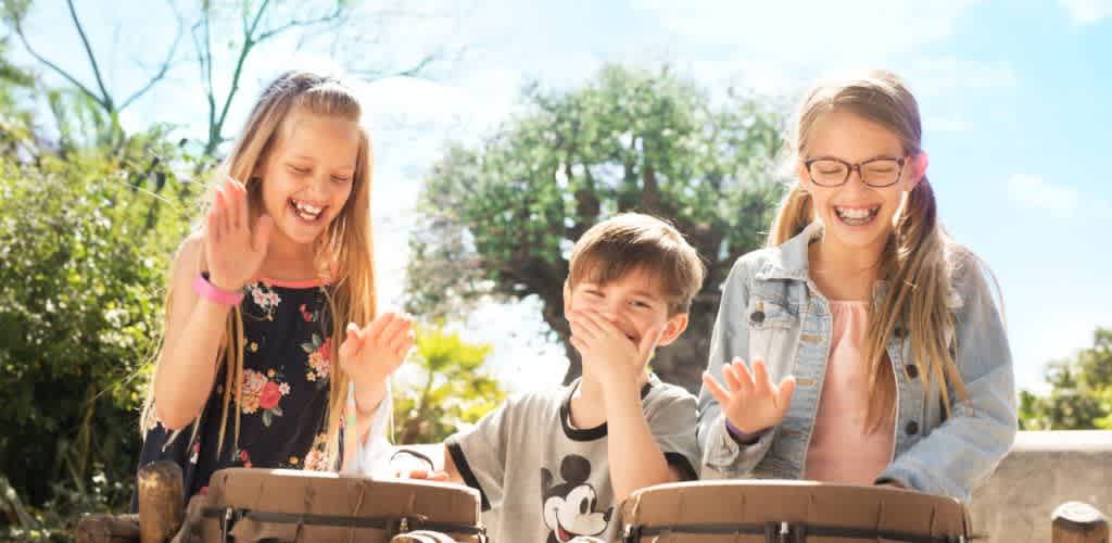 Three children laughing and enjoying outdoors on a sunny day with trees in the background