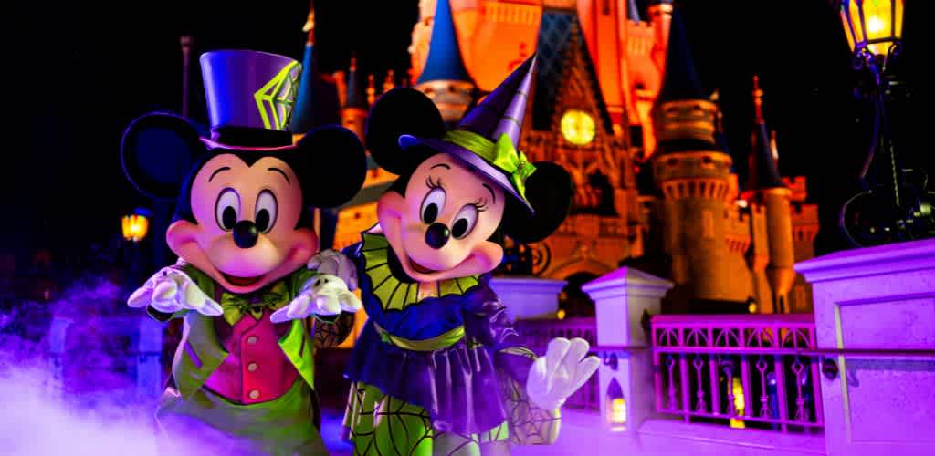 Mickey Mouse and Minnie Mouse dressed as Halloween characters at a Disney castle with colorful lighting and fog effects.
