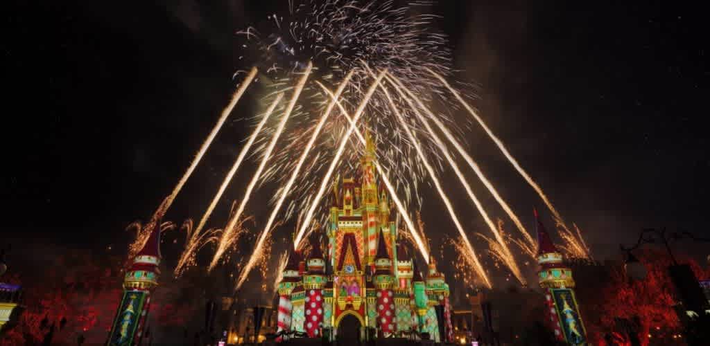 Fireworks explode above a colorful castle during a nighttime celebration at a Disney park.