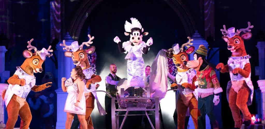 Costumed reindeer and a cow perform on stage with a magician, surrounded by colorful lights and theatrical props in a festive holiday show setting.