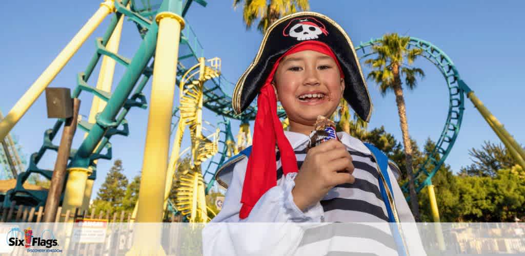 Child in a pirate costume in front of a roller coaster at an amusement park.