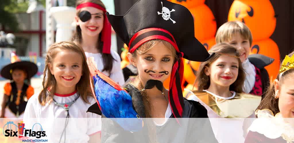 Group of children in Halloween costumes, including a pirate and nurse, at an outdoor event with inflatable pumpkins in the background.