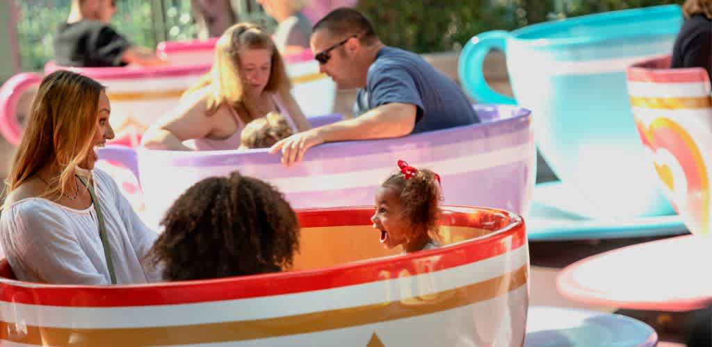 Happy children and adults enjoying rides in colorful teacup amusement park attractions outdoors.