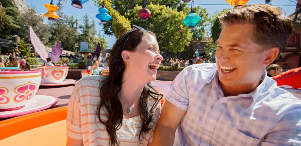 Two smiling people enjoying a colorful amusement park ride outdoors on a sunny day.