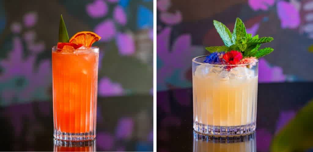 Two refreshing cocktails sit on a colorful background. The left drink is bright orange with a slice of citrus and a green leaf garnish. The right drink is a pale yellow with ice, topped with vibrant mint leaves and colorful flower garnishes. Both are served in clear glass tumblers. The vivid backdrop features hues of pink and purple, adding a lively atmosphere.