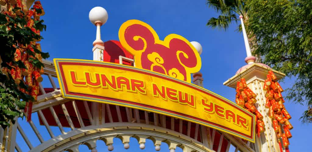 Festive entrance adorned with a bright yellow and red sign reading Lunar New Year. Decorative lanterns hang on either side of the archway. The design features symbolic swirls and shapes, with trees and a sunny blue sky in the background, creating a joyful and welcoming atmosphere.