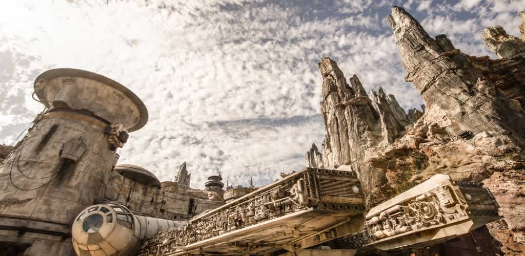 A futuristic, starship-themed attraction set against a rugged mountain landscape. The structure features intricate mechanical details and a spacecraft design, with a cloudy sky above. The scene evokes adventure and fantasy, inviting visitors into an imaginative world of exploration.