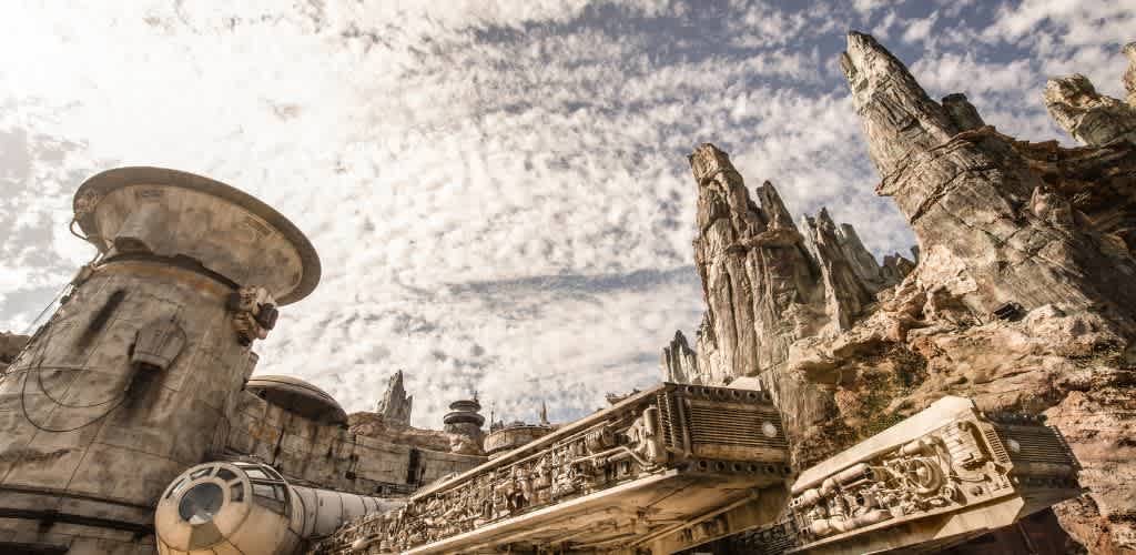 A futuristic spacecraft rests in an otherworldly, rocky landscape. The structure features intricate details and weathered textures. Towering spires and rugged formations rise against a sky filled with scattered clouds, creating an adventurous and cinematic atmosphere.