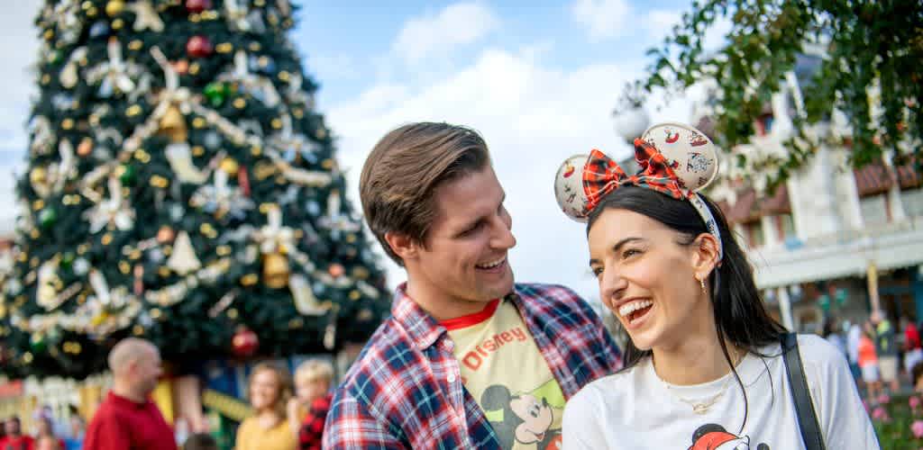 A smiling couple enjoying a festive outdoor event with decorated Christmas trees and holiday attire.