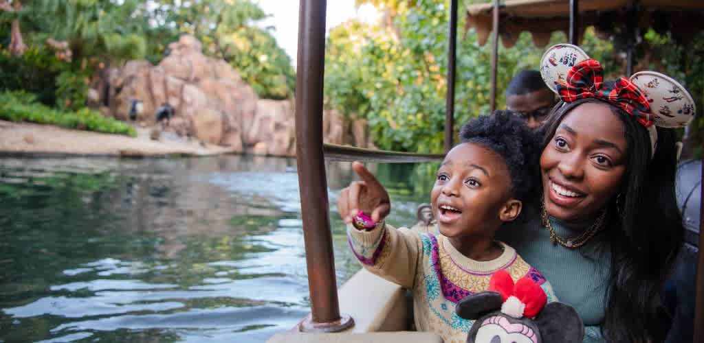 A joyful mother and child on a boat ride at a zoo or park, enjoying the water and surrounded by trees and wildlife.