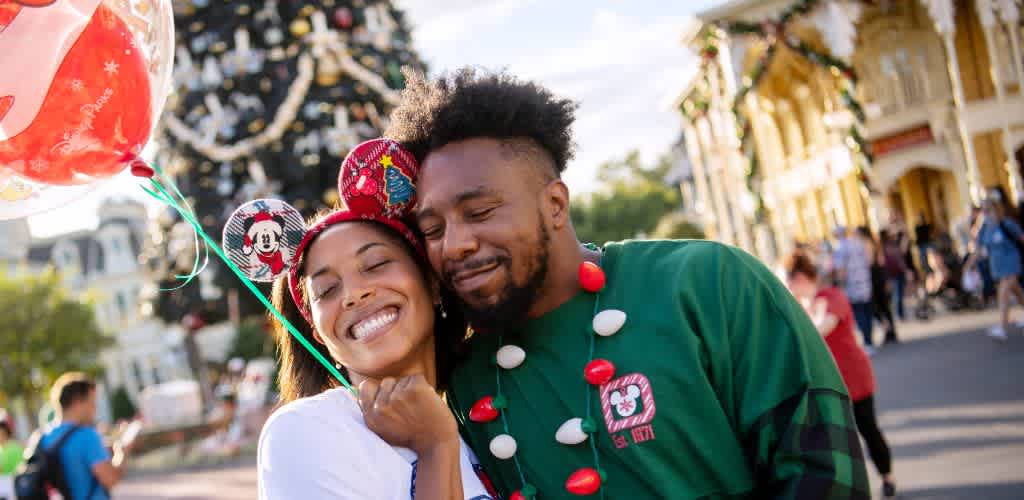 A smiling couple enjoying a festive outdoor event with decorations and a decorated Christmas tree in the background.