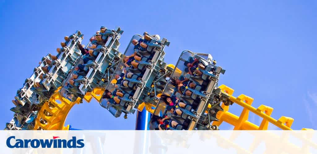 An exhilarating roller coaster at Carowinds amusement park, captured in motion with its riders secured in seats on a yellow and blue track, against a backdrop of clear blue sky.