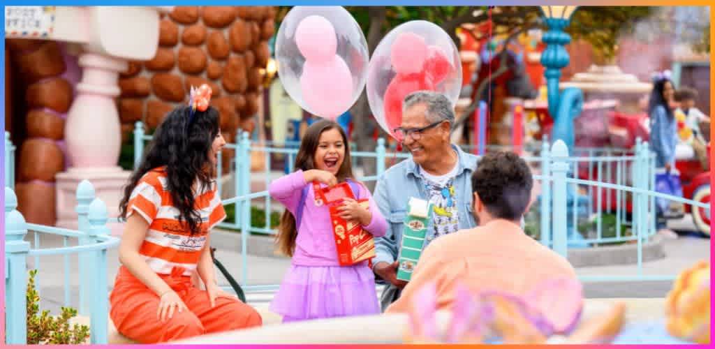 Children and an adult enjoy smiling outdoors with balloons, gifts, and colorful amusement park surroundings.