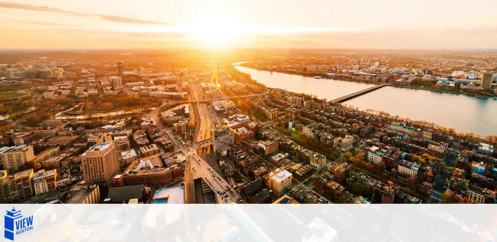 Aerial view of a cityscape at sunset with a river, bridge, and urban buildings.