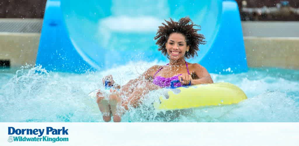 Woman riding a yellow inner tube down a blue water slide, smiling.