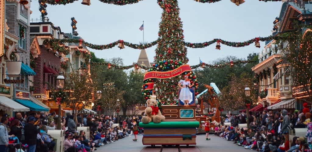 A large decorated Christmas tree on a parade float with people walking and sitting on both sides in a festive holiday scene