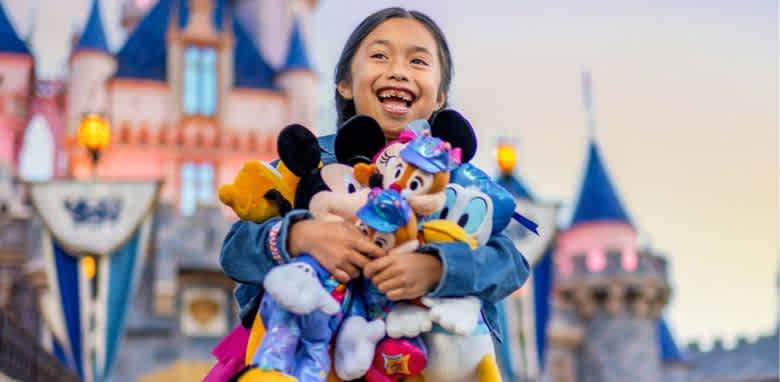 A joyful child stands in front of a colorful castle, grinning widely and embracing a collection of plush toys featuring popular cartoon characters. The scene captures a sense of happiness and excitement, enhanced by the vibrant backdrop of the whimsical castle and softly glowing lights.