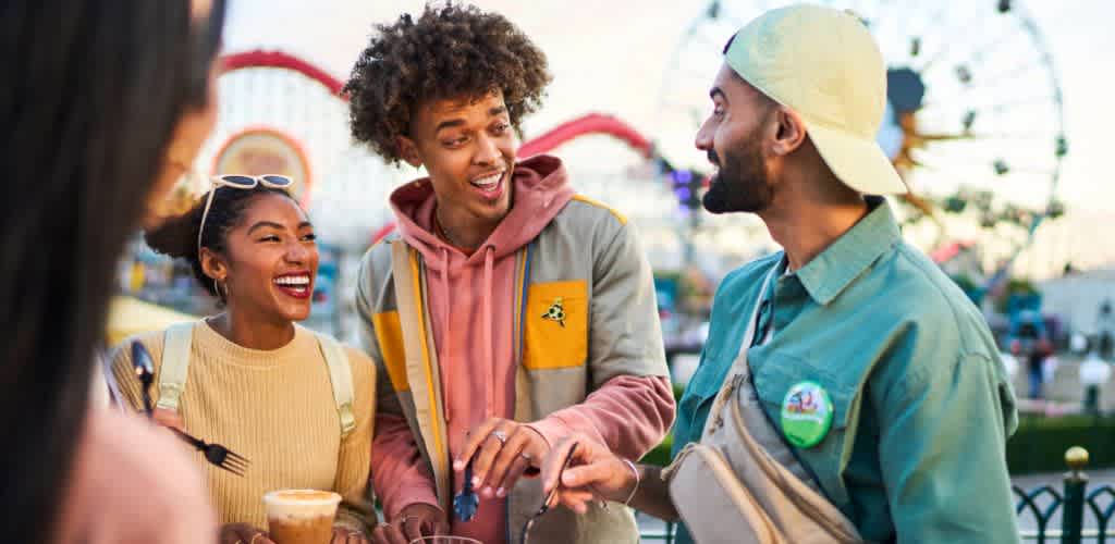 A joyful group of three friends enjoy a lively time at an amusement park. They are chatting and laughing together while sharing a food experience. In the background, you can see a ferris wheel and colorful rides, suggesting a vibrant and fun atmosphere perfect for celebrating special moments.