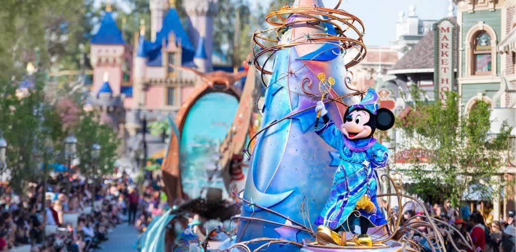 Mickey Mouse dressed as a sorcerer riding on a decorated parade float at a Disney theme park with a castle in the background