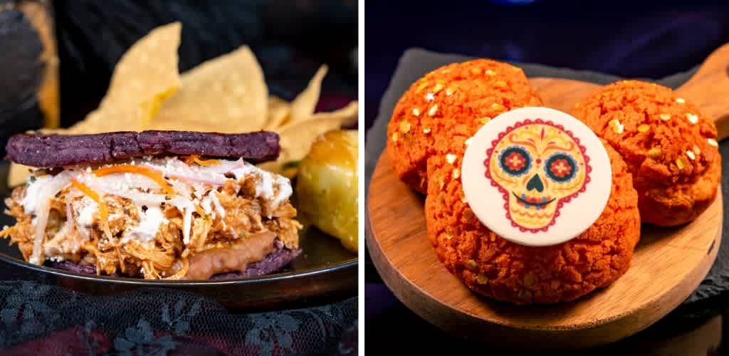 Side view of a pulled pork sandwich with potato chips and pickles on a black plate and a wooden platter with three decorated sugar cookies featuring a colorful skull design.