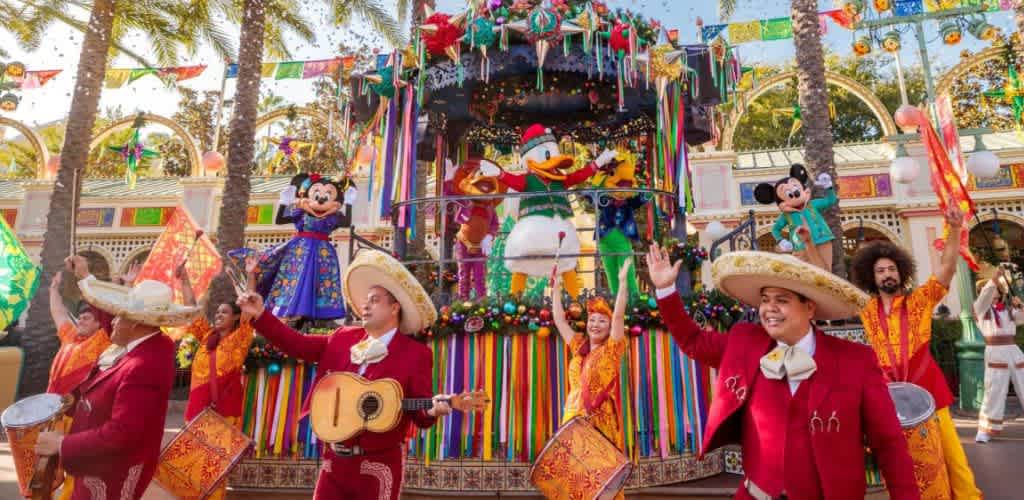 Colorful parade float with Disney characters and performers in traditional Mexican attire celebrating a festive event outdoors.
