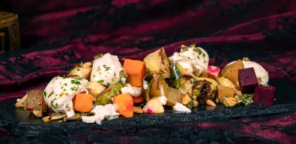 Poached eggs served with roasted vegetables, beets, and herbs on a dark rectangular plate with a velvet red and black cloth background.