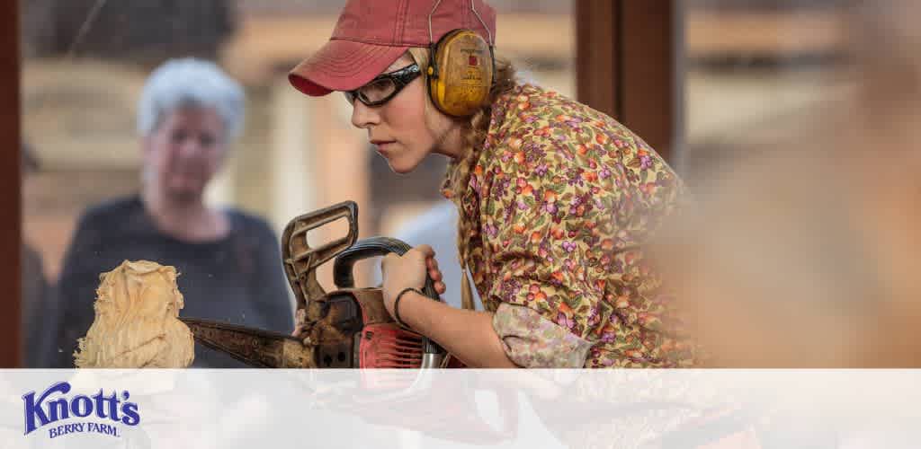 This image depicts an individual engaging in a wood carving activity using a chainsaw. The person is wearing protective gear, which includes a pair of clear safety glasses and ear protection. They are intently focused on their task, carving a figure from a light-colored piece of wood. In the background, another individual appears to be observing the wood carving process. The setting suggests that this is a live demonstration at Knott's Berry Farm, as indicated by the logo at the bottom of the image.

Discover the artistry and craftsmanship of wood carving on your next visit to Knott's Berry Farm, and remember to check out FunEx.com for the lowest prices and best discounts on tickets!