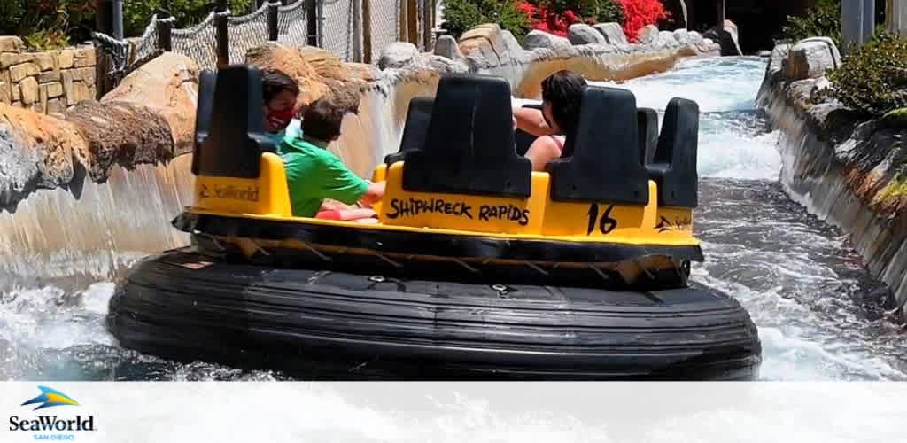 A vibrant photo of visitors at SeaWorld San Diego enjoying a thrilling ride on the Shipwreck Rapids. Guests in a round, yellow raft numbered 16 splash through the churning water of a rapids course on a sunny day, evoking the excitement of an adventurous river expedition.