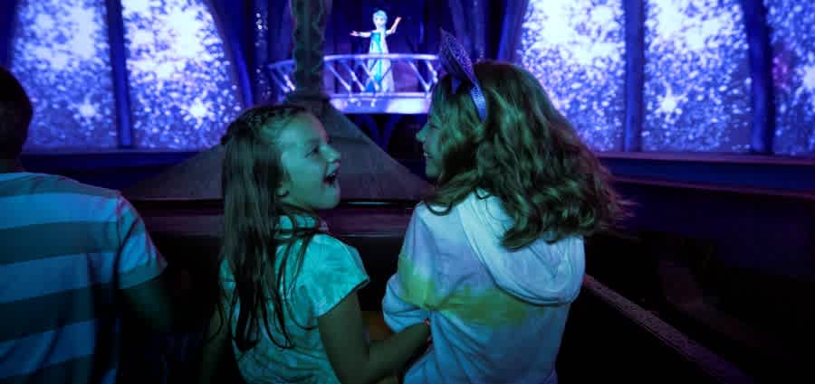 Two young friends laugh with excitement as they embark on a whimsical journey through a Frozen-inspired attraction.
