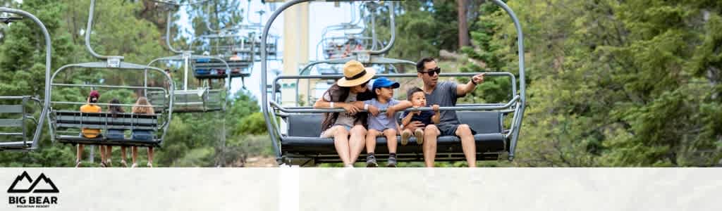 Image of a family enjoying a scenic chairlift ride at Big Bear. A man points out something in the distance to a child seated next to a woman wearing a wide-brimmed hat. Lush green trees form the backdrop, and the Big Bear logo is visible at the bottom.