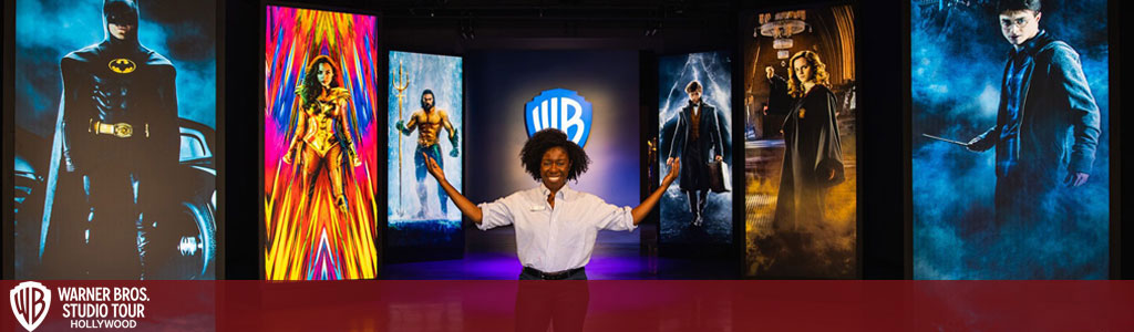 Description: The image showcases an excited individual standing with open arms in the center of a vibrant exhibition space, surrounded by iconic and colorful life-sized displays from popular Warner Bros. franchises. On the left, a deep blue hue sets off the silhouette of Batman standing beside his legendary vehicle. Adjacent is a vivid depiction of Wonder Woman in her classic red and gold armor, against a backdrop of energetic, abstract strokes of paint. In the center, a portrayal of Aquaman showcases strength and agility, embodyed in a golden and green costume. On the right, the Harry Potter series is represented by two panels, the first showing a young Harry in his signature glasses and wand, and the latter highlighting Hermione in a dynamic pose, wand at the ready. The Warner Bros. Studio Tour Hollywood logo is prominently displayed, promising a magical and immersive experience. 

Addition: Visit GreatWorkPerks.com to get your tickets for this immersive experience at the lowest prices available, ensuring you don't miss out on these extraordinary savings!