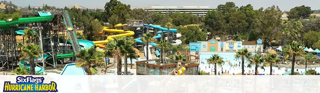 This image showcases a vibrant and lively water park under the clear blue sky. The foreground presents an array of colorful water slides, some encased in tubes and others open-air, winding and twisting in various directions, all surrounded by lush green palm trees. Below, the water park features a large, bustling swimming area where guests can be seen enjoying the cool water. The midground consists of buildings with turquoise-colored roofs, which appear to be facilities for the convenience of the visitors, such as changing rooms or eateries. In the background, we can notice a flat expanse and more greenery, indicating the park is situated in a spacious and possibly suburban environment. The top left of the image prominently displays the Six Flags Hurricane Harbor logo.

Embark on a splash-tastic adventure and soak up the savings with our lowest prices on tickets to this aquatic paradise, only at GreatWorkPerks.com.