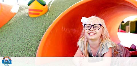 Girl with glasses smiling at end of playground slide.