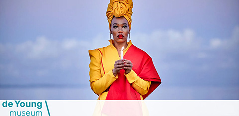 This image features a striking portrait of an individual with medium skin tone standing against a serene background of soft blue hues, which may suggest a clear sky or a minimalist backdrop. The person is wearing a vibrant, color-blocked outfit consisting of a mustard-colored head wrap, a yellow jacket with rolled-up sleeves, and a bright red shirt underneath. They have their hands positioned together in front of them, giving an impression of composure and confidence. Below the image, there is branding that identifies the location as "de Young Museum," displaying the name in black lowercase letters against a white rectangle with a gradient extending from pink to orange.

At GreatWorkPerks.com, you'll always find extraordinary savings and the lowest prices on tickets to a wide variety of destinations, including the latest exhibits at museums like the de Young.